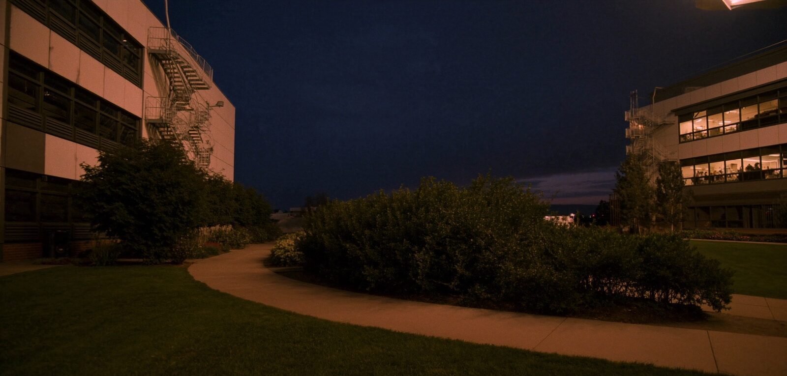 A quiet research-campus quad with modern laboratory buildings glowing at blue hour