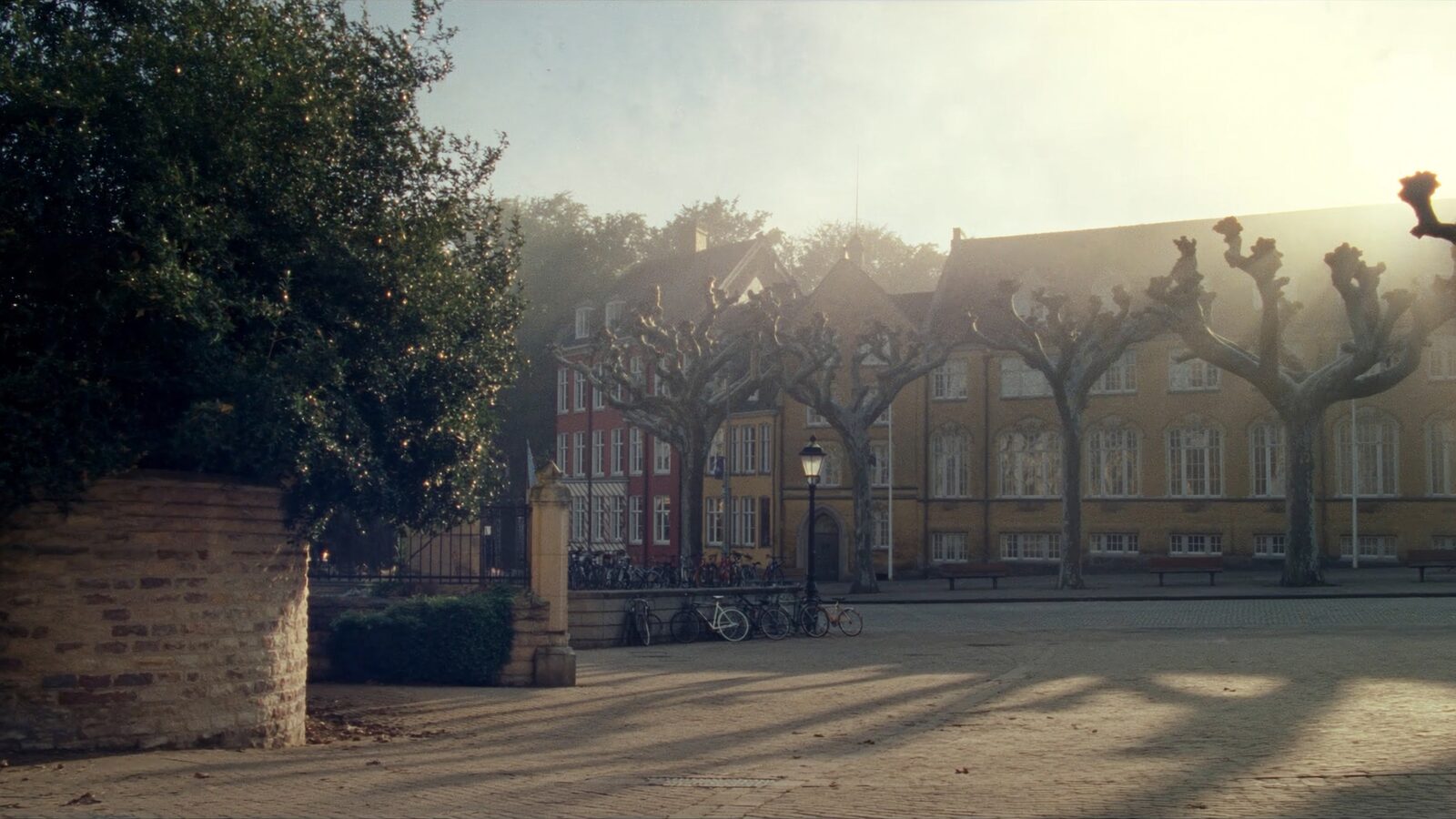 Empty cobbled square in a European university town at dawn with brick buildings, bicycles, and bare autumn trees