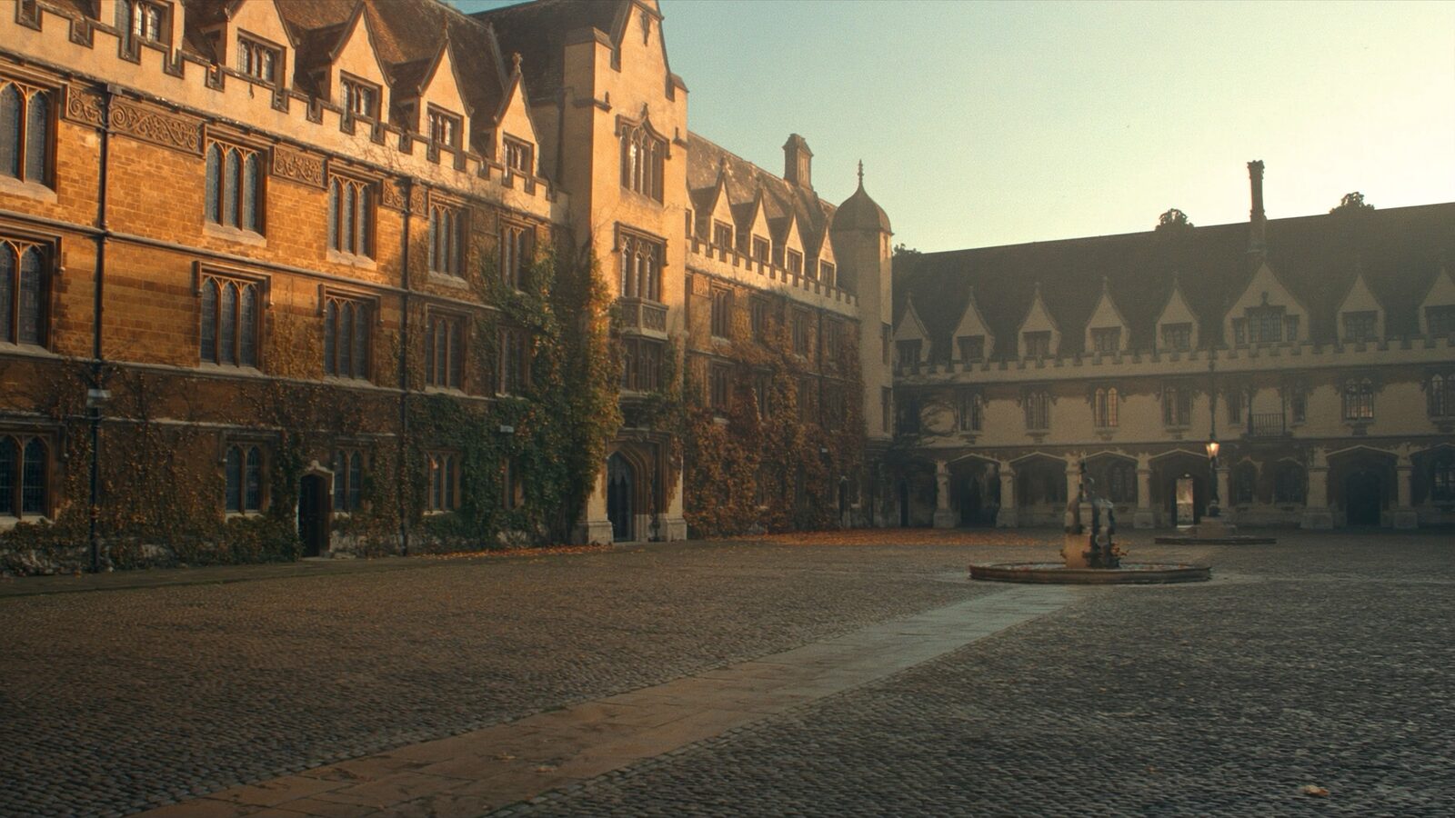 Empty stone quadrangle of a historic British university at golden hour with ivy covered gothic walls and cobbled ground