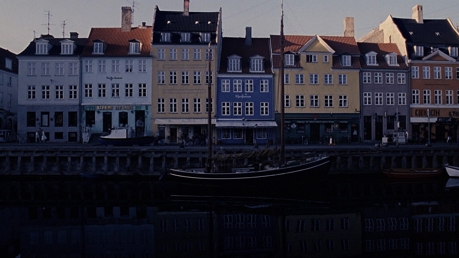 Copenhagen's Nyhavn canal at dusk with colorful townhouses reflected in still water and moored boats along an empty quay