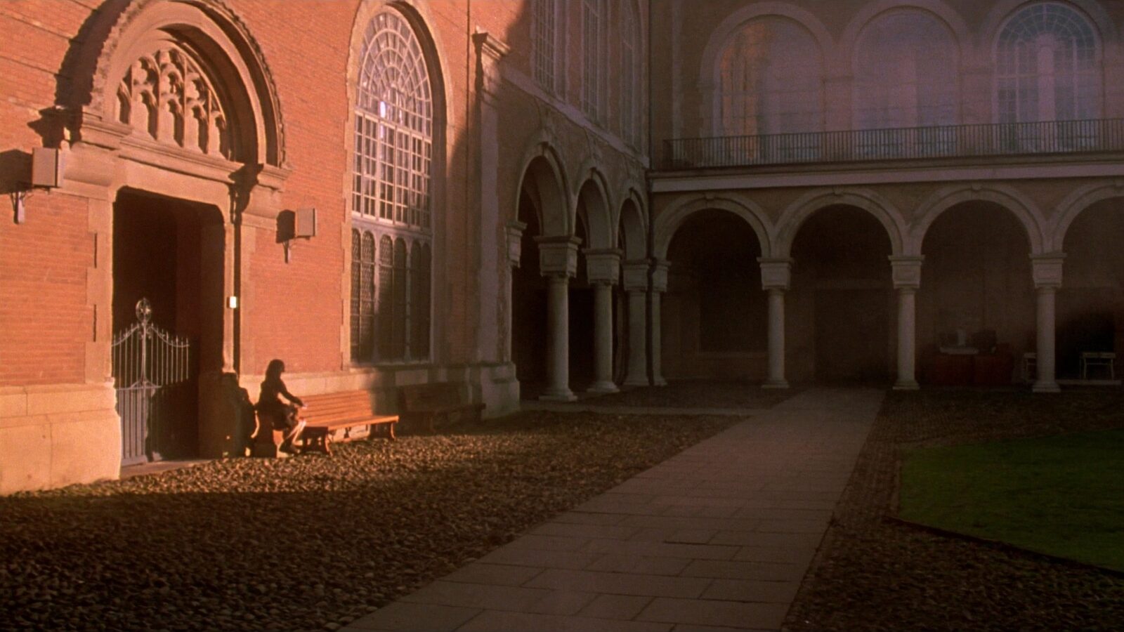 Empty arched stone courtyard of a European university at dawn with long shadows across cobblestones