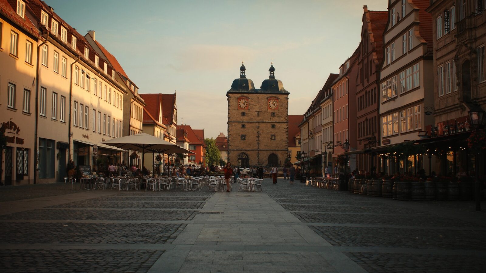 A bright German city square with classic facades and empty cafe terraces at golden hour