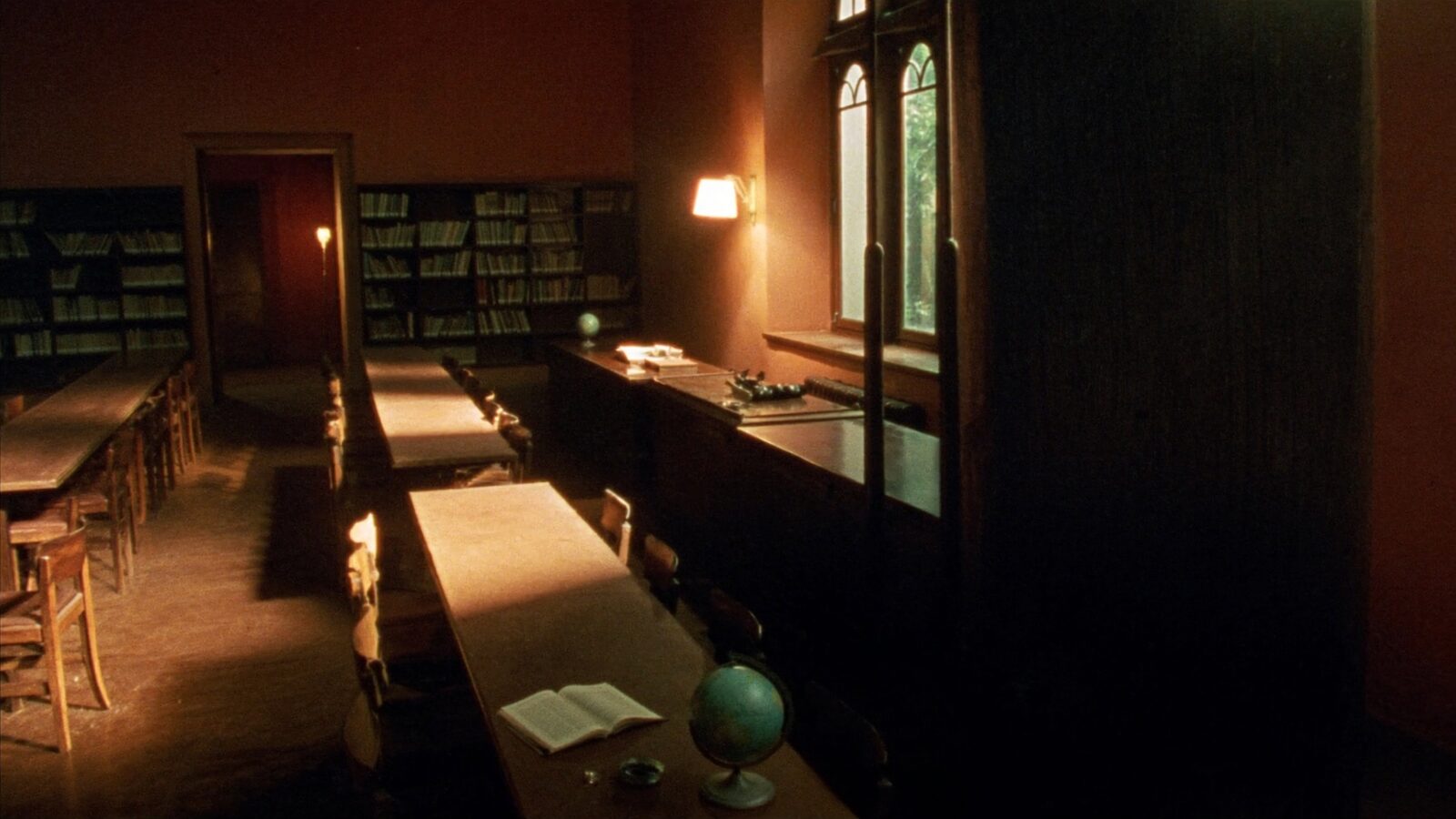 Empty sunlit university library reading room with long study tables and tall windows