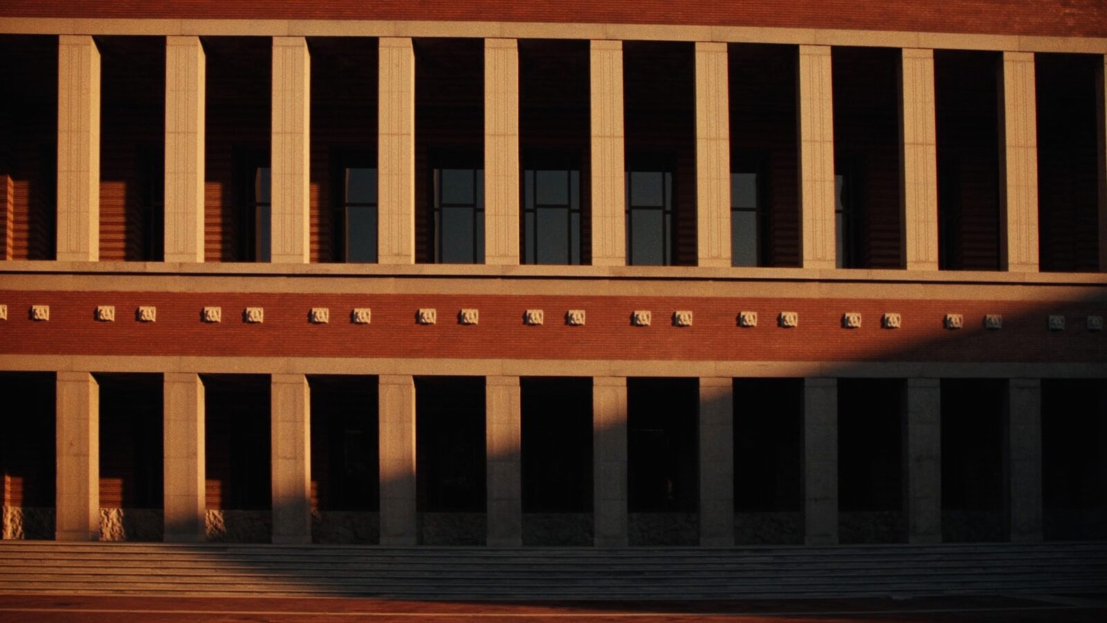 An empty stone colonnade of a government building at golden hour, long steady shadows across granite steps.