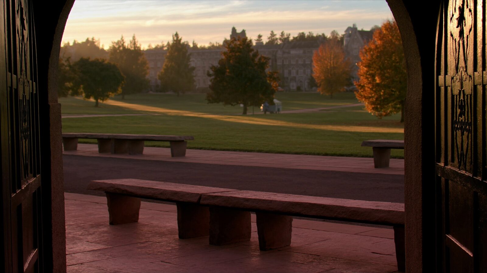 Empty university quad at dawn viewed through a stone archway with long shadows and autumn trees