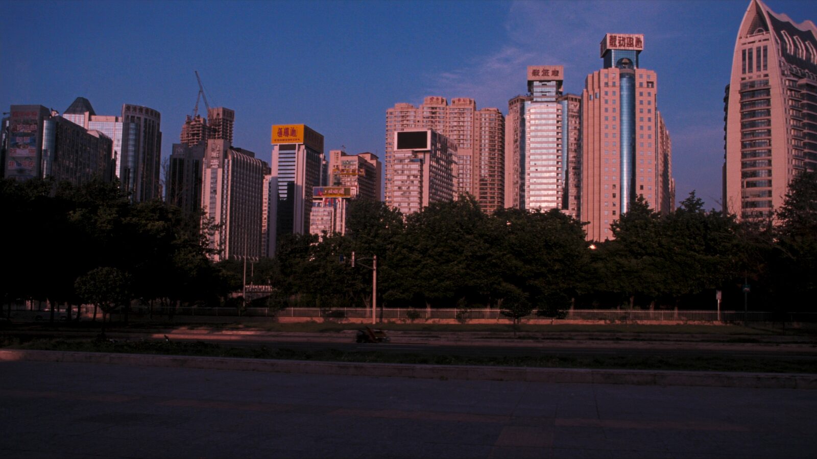 A modern East Asian city skyline of glass towers under a deep blue dusk sky