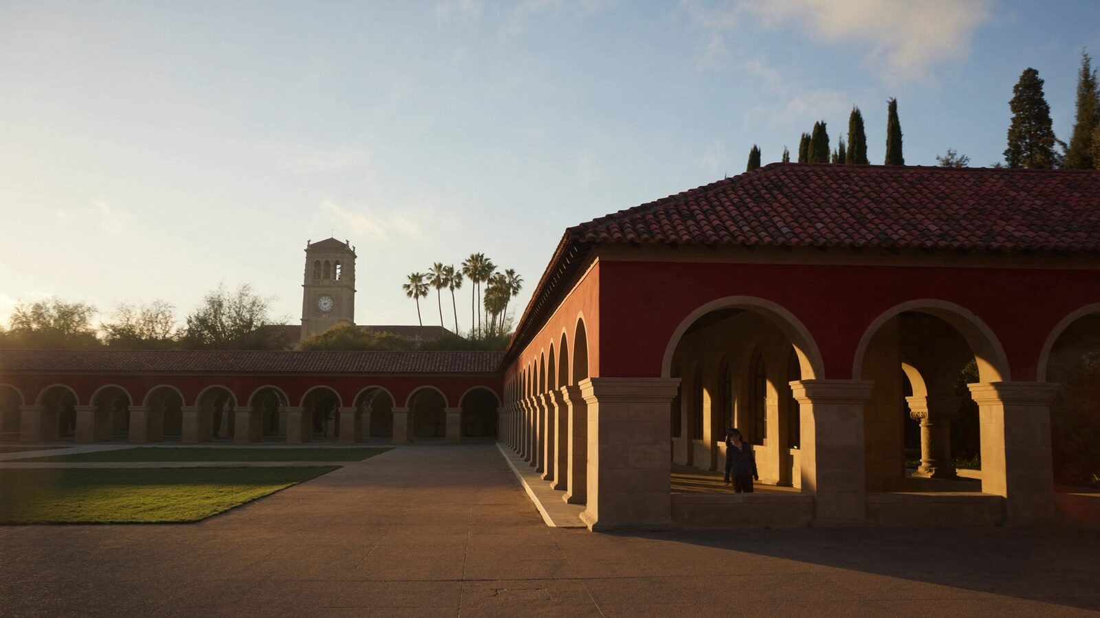 Sandstone university arcades and palm-lined walkway leading to a bell tower at golden hour