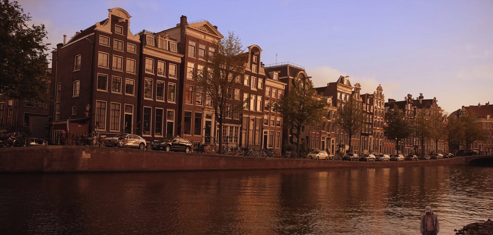 An Amsterdam canal lined with tall narrow gabled houses and bicycles at golden hour