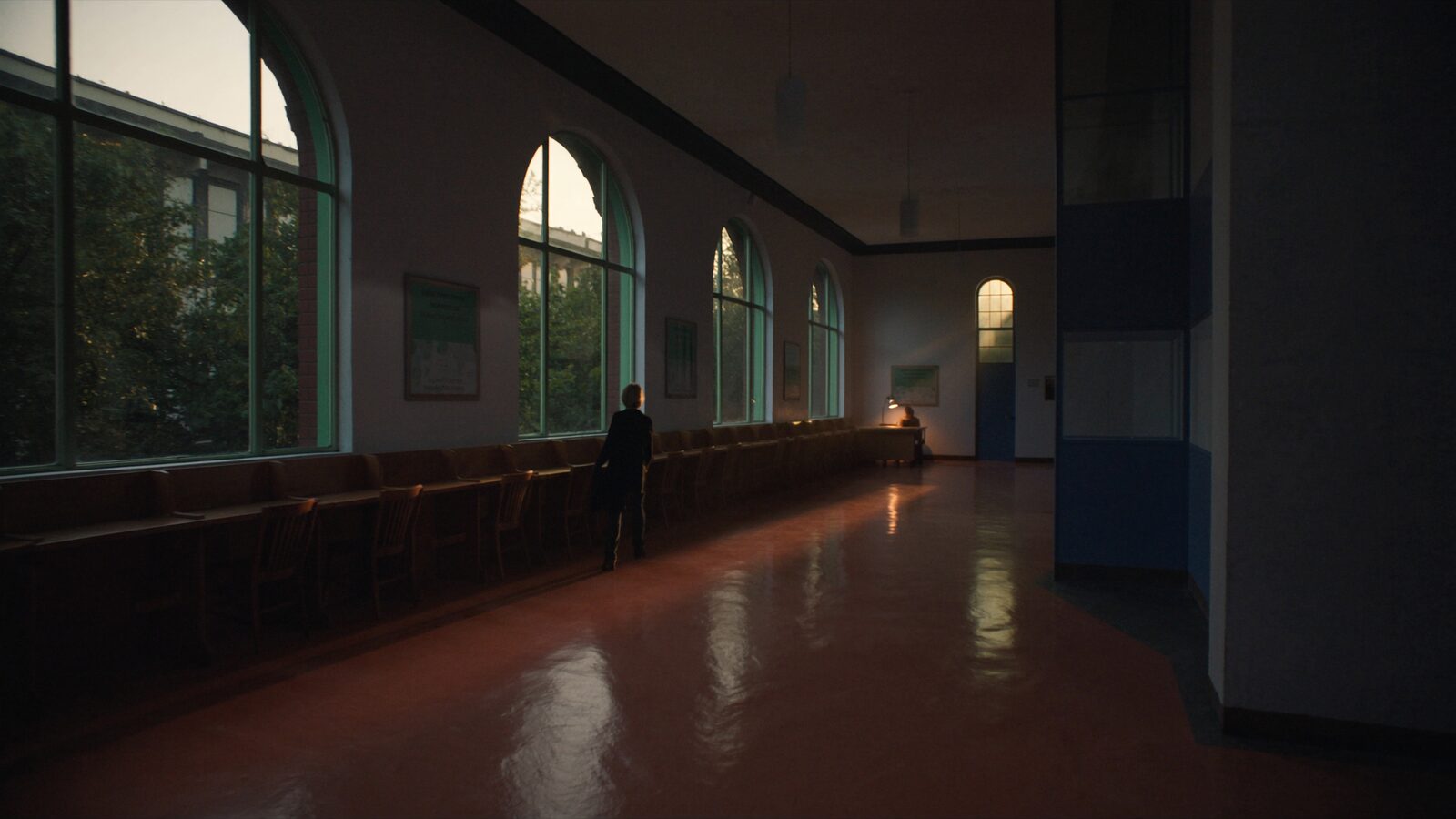 An empty dusk-lit university research corridor with arched windows and a single lamp glowing at the far end