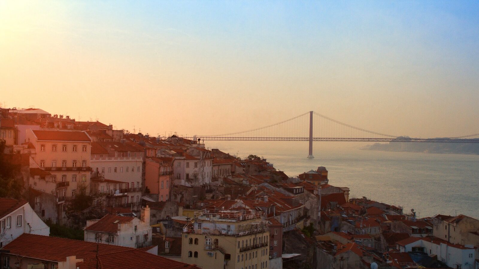 Aerial view of Lisbon's terracotta rooftops sloping down to the Tagus river at dawn