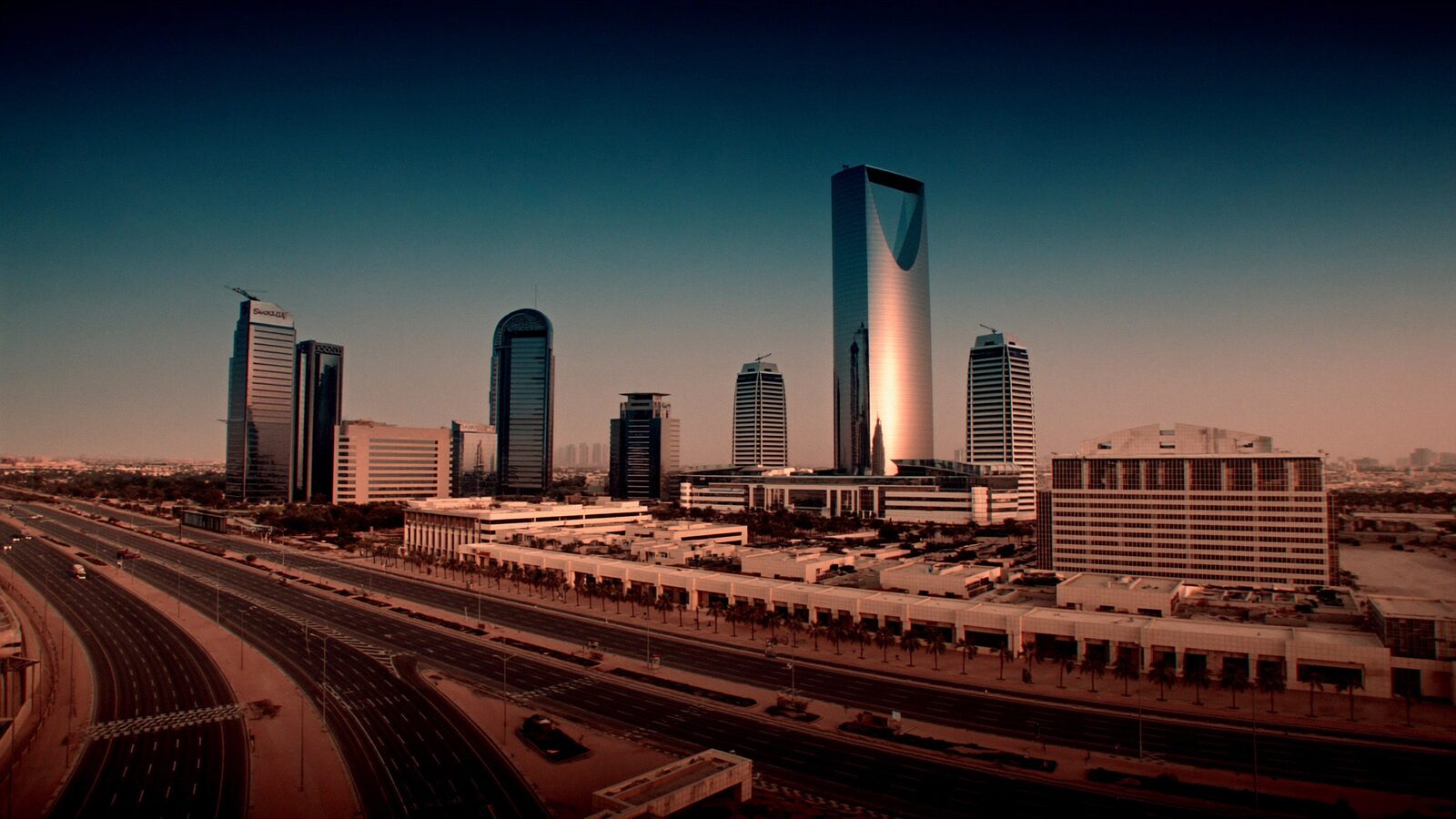 Riyadh skyline of glass towers at dusk with palm-lined boulevards under a clear desert sky
