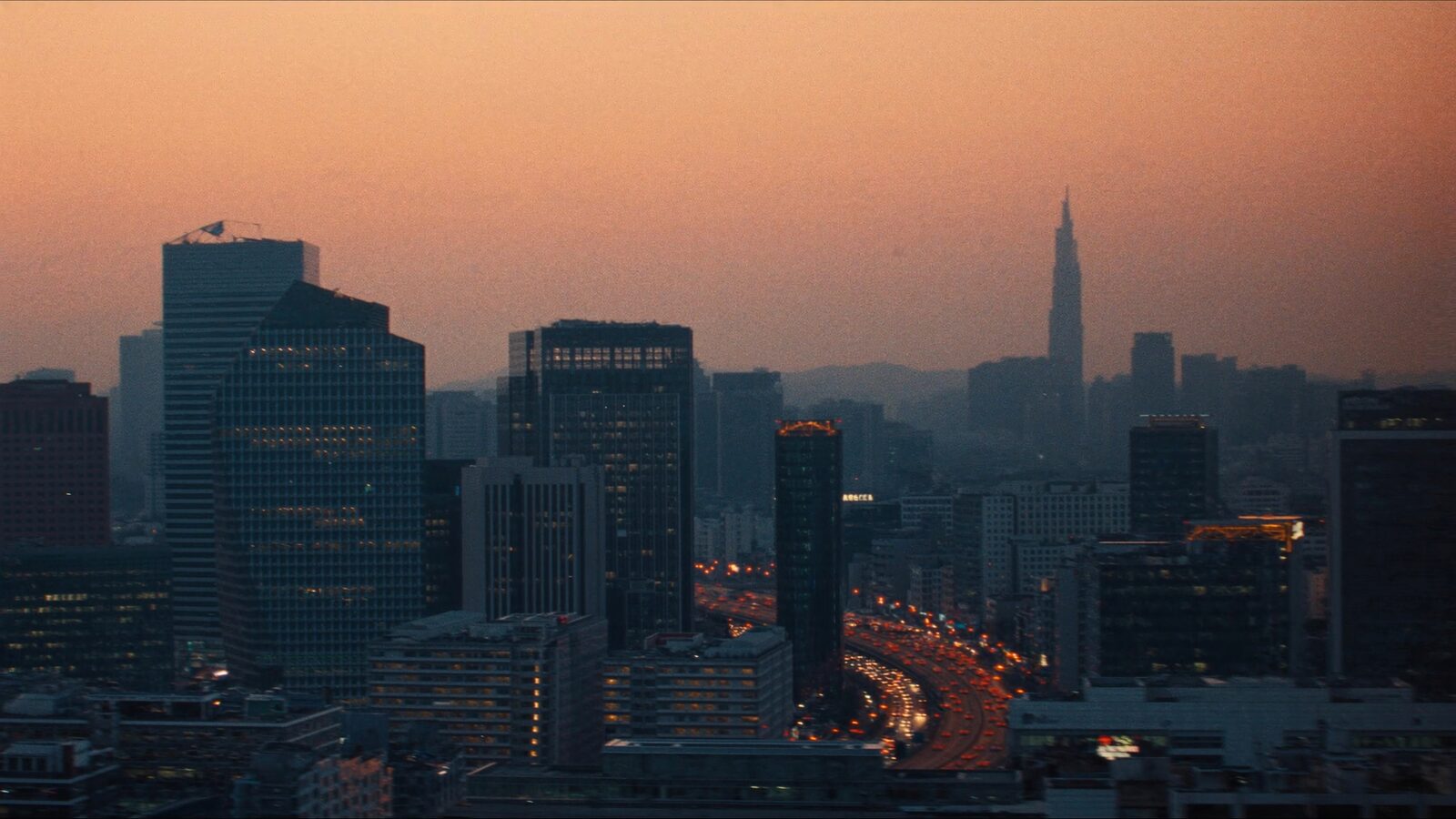 Dusk aerial view of Seoul's southern tech district with glass towers and lit expressways below hazy mountains