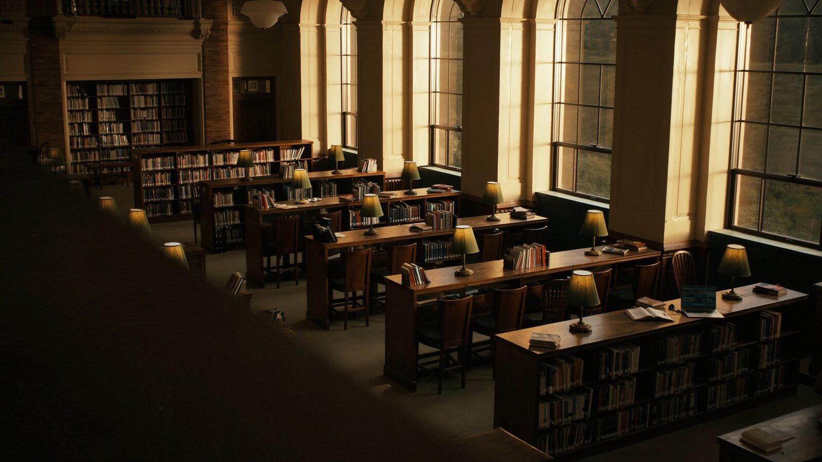 Empty golden-hour university library reading room with study desks and tall arched windows