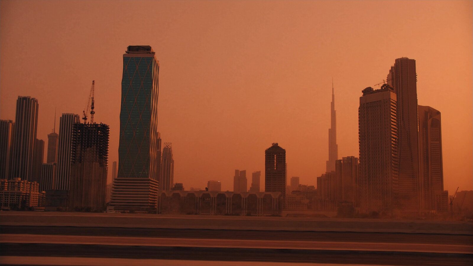 A Dubai skyline of sleek glass towers under a warm desert dusk haze