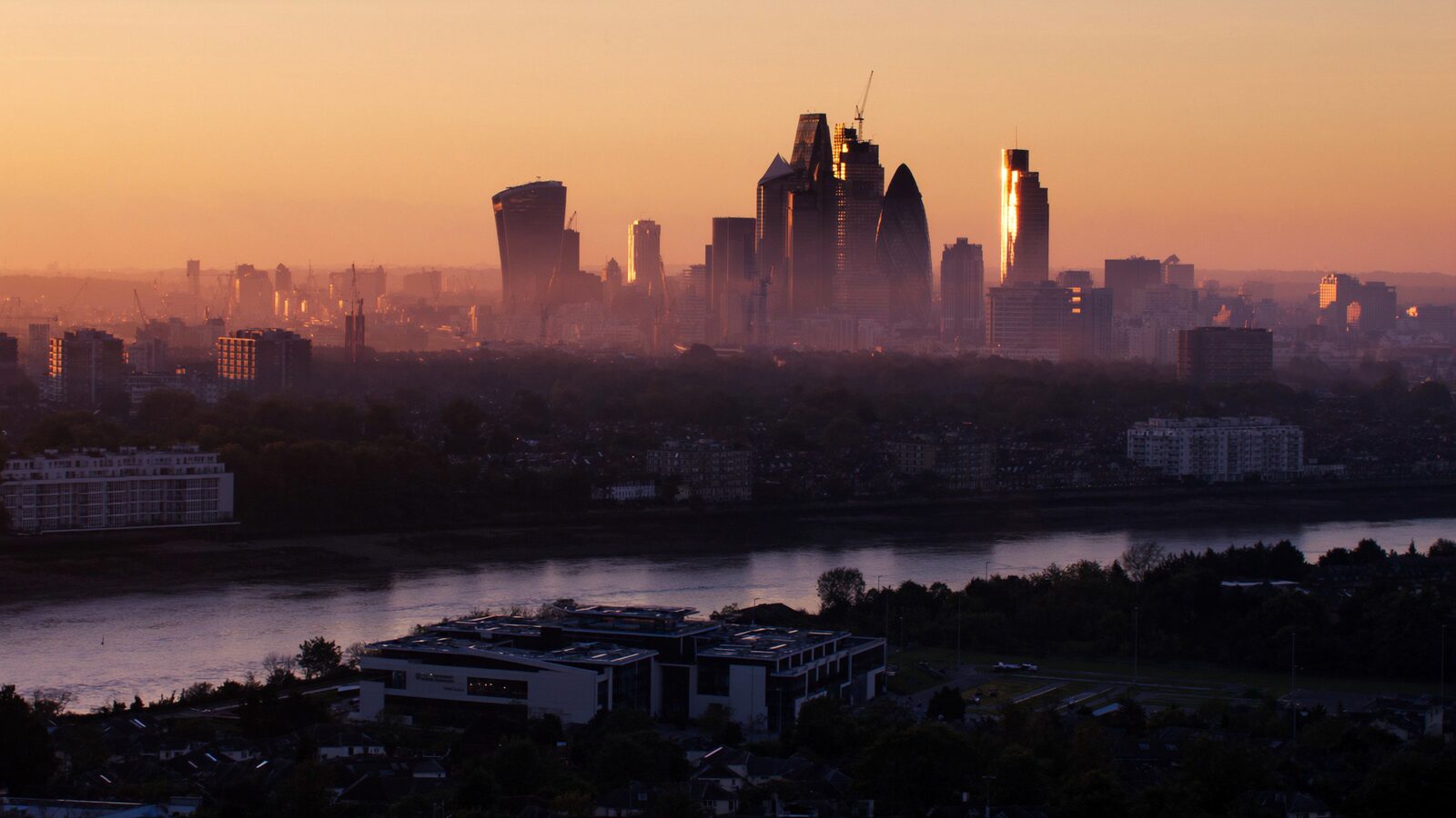 London skyline along the Thames at dawn with glass office towers in soft golden light