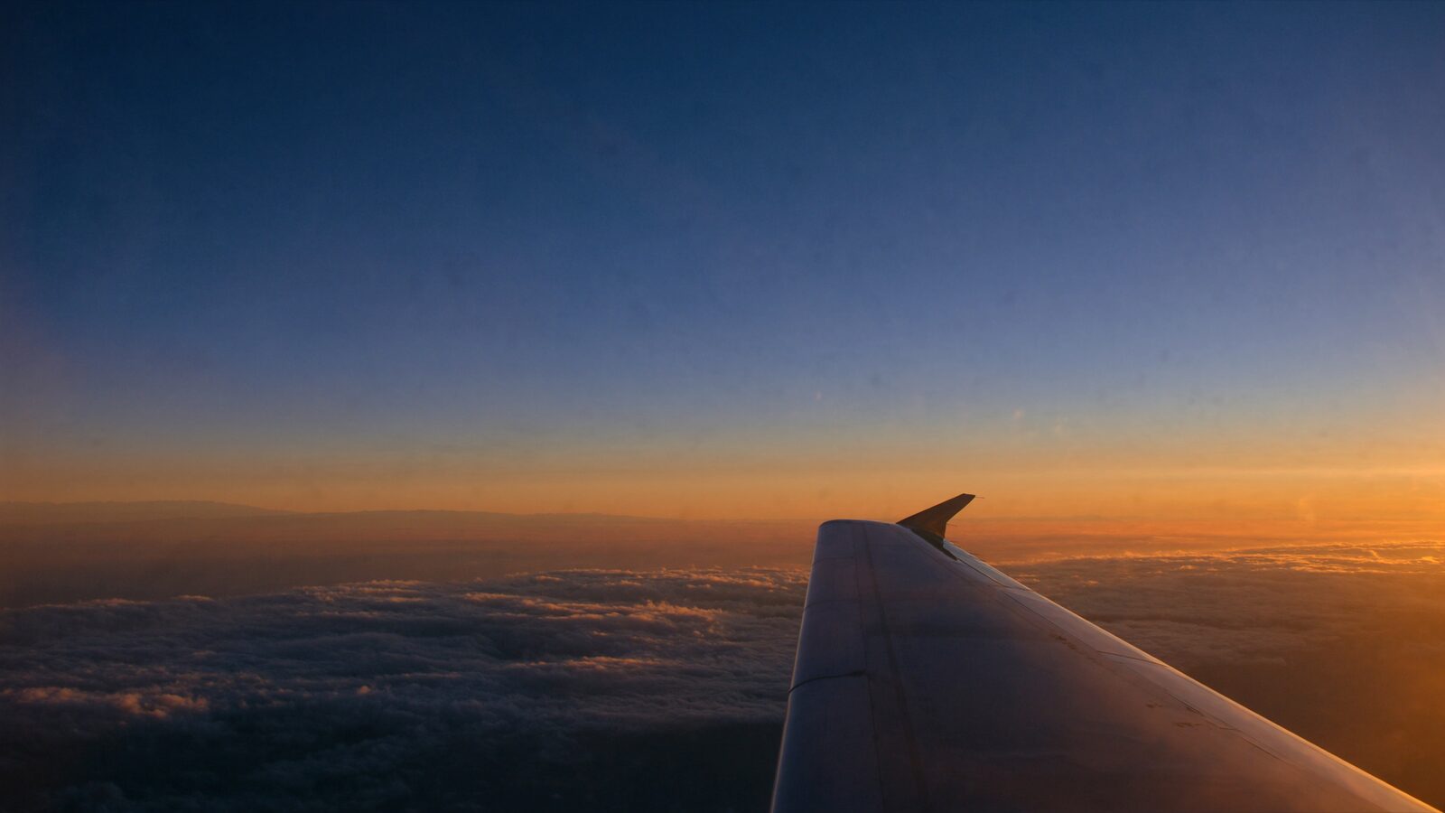 A plain aircraft wing above a golden cloud deck over the Atlantic at sunrise.