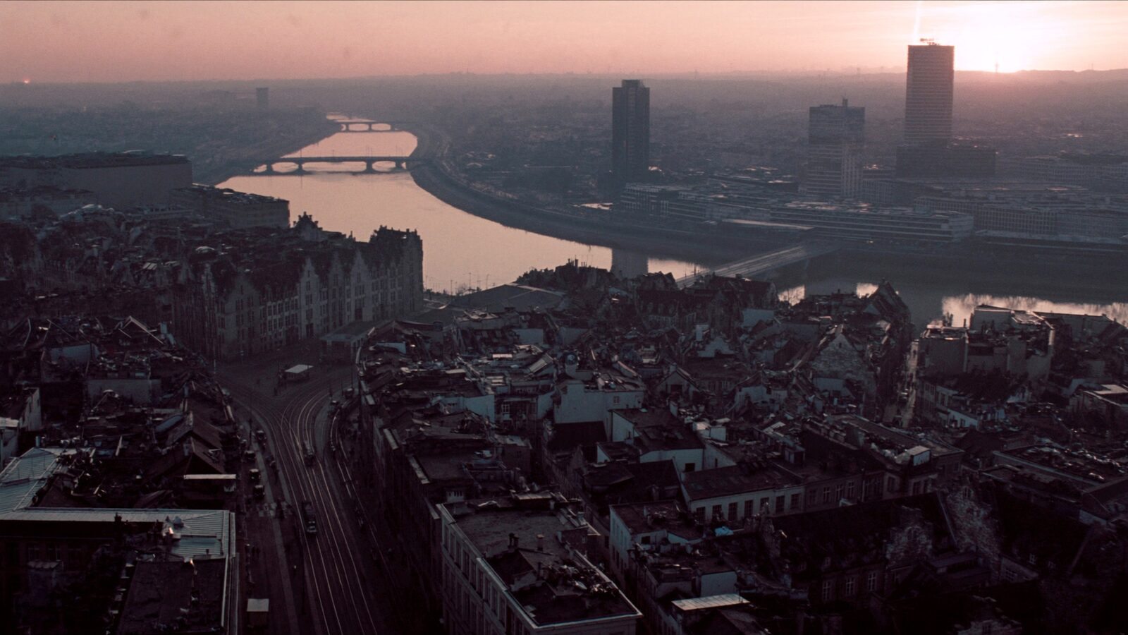 Aerial dusk view of a European city divided by a river, historic rooftops on one side and glass towers on the other